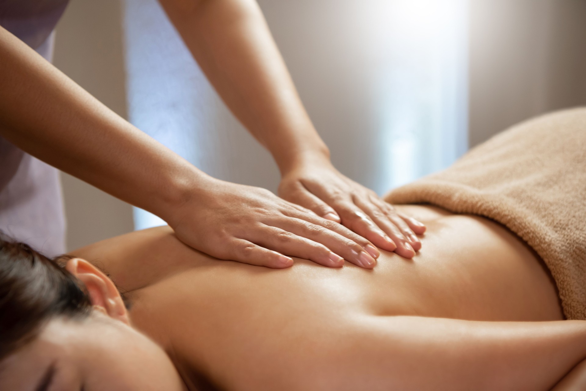 Masseuse doing massage on Asian female body in the spa salon.